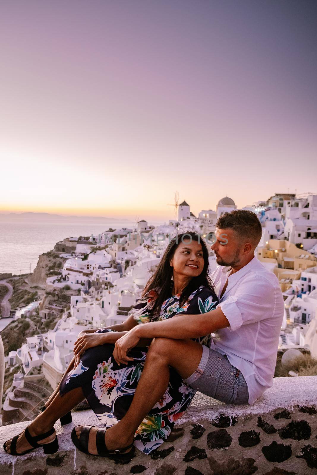 Santorini Greece, young couple on luxury vacation at the Island of Santorini watching sunrise by the blue dome church and whitewashed village of Oia Santorini Greece during sunrise, men and woman on holiday in Greece by fokkebok