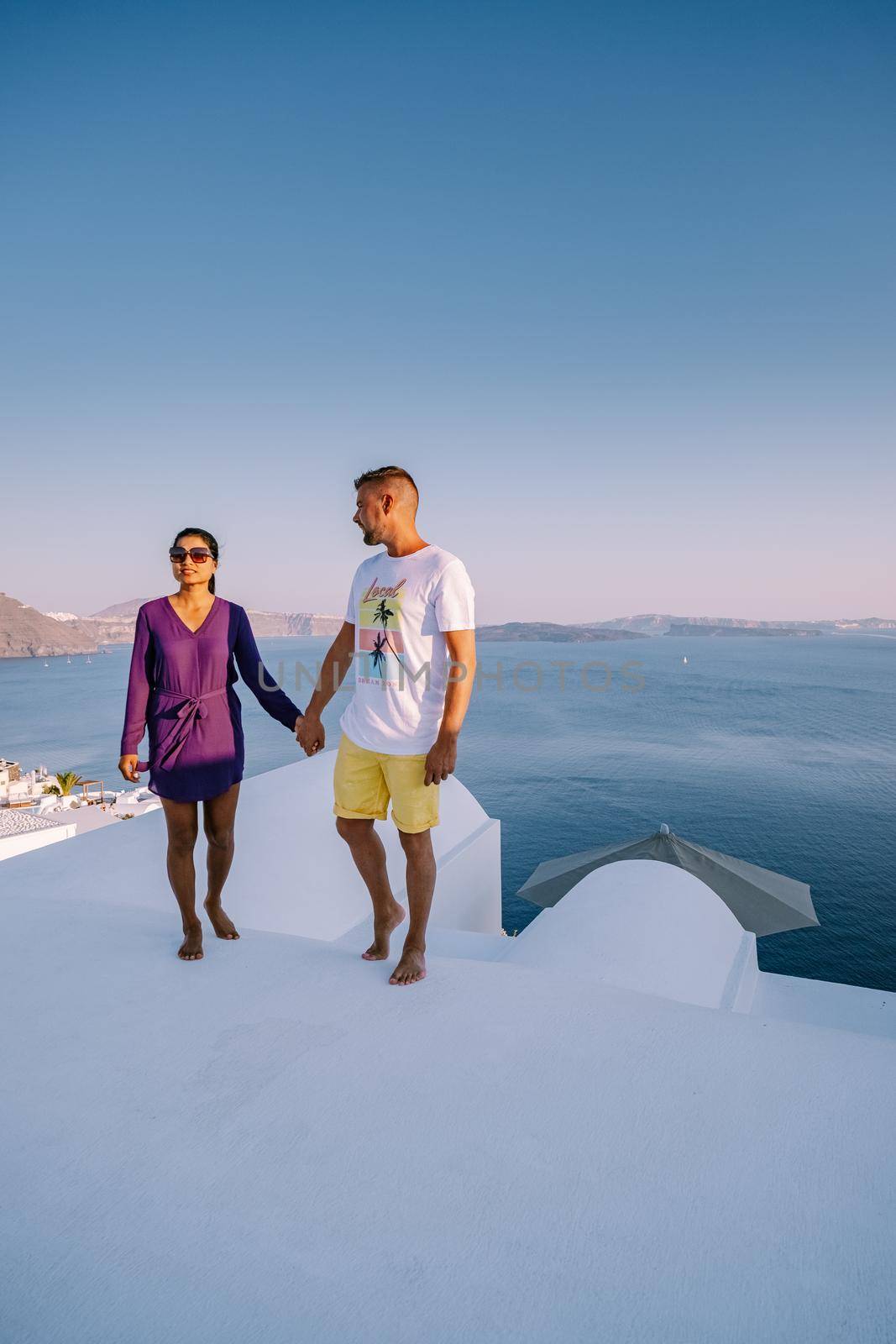 Santorini Greece, young couple on luxury vacation at the Island of Santorini watching sunrise by the blue dome church and whitewashed village of Oia Santorini Greece during sunrise, men and woman on holiday in Greece by fokkebok