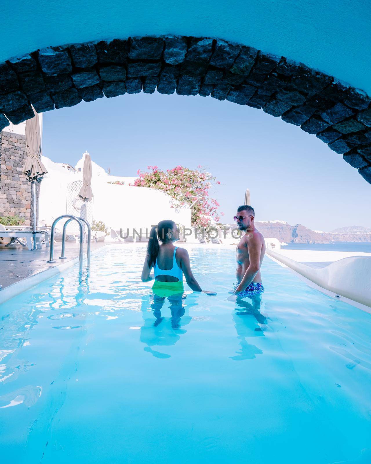 Santorini Greece, young couple on luxury vacation at the Island of Santorini watching sunrise by the blue dome church and whitewashed village of Oia Santorini Greece during sunrise, men and woman on holiday in Greece by fokkebok