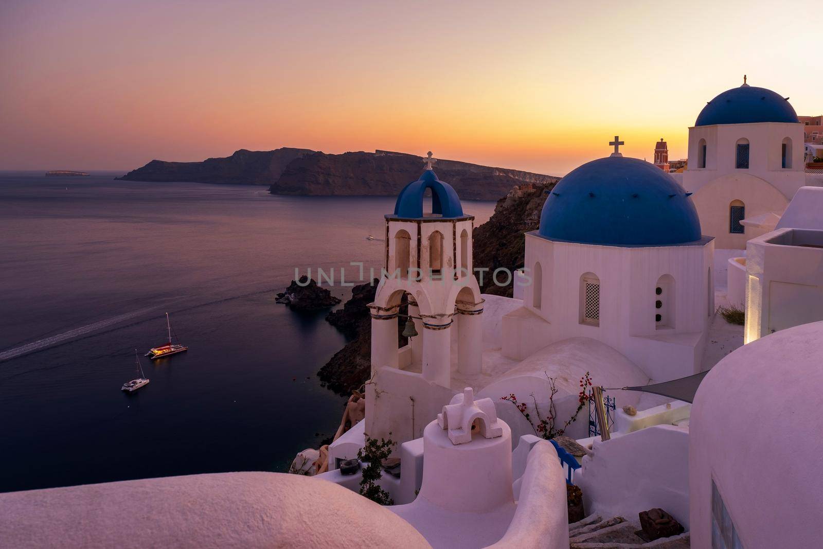 Sunset at the Island Of Santorini Greece, beautiful whitewashed village Oia with church and windmill during sunset, streets of Oia Santorini during summer vacation at the Greek Island