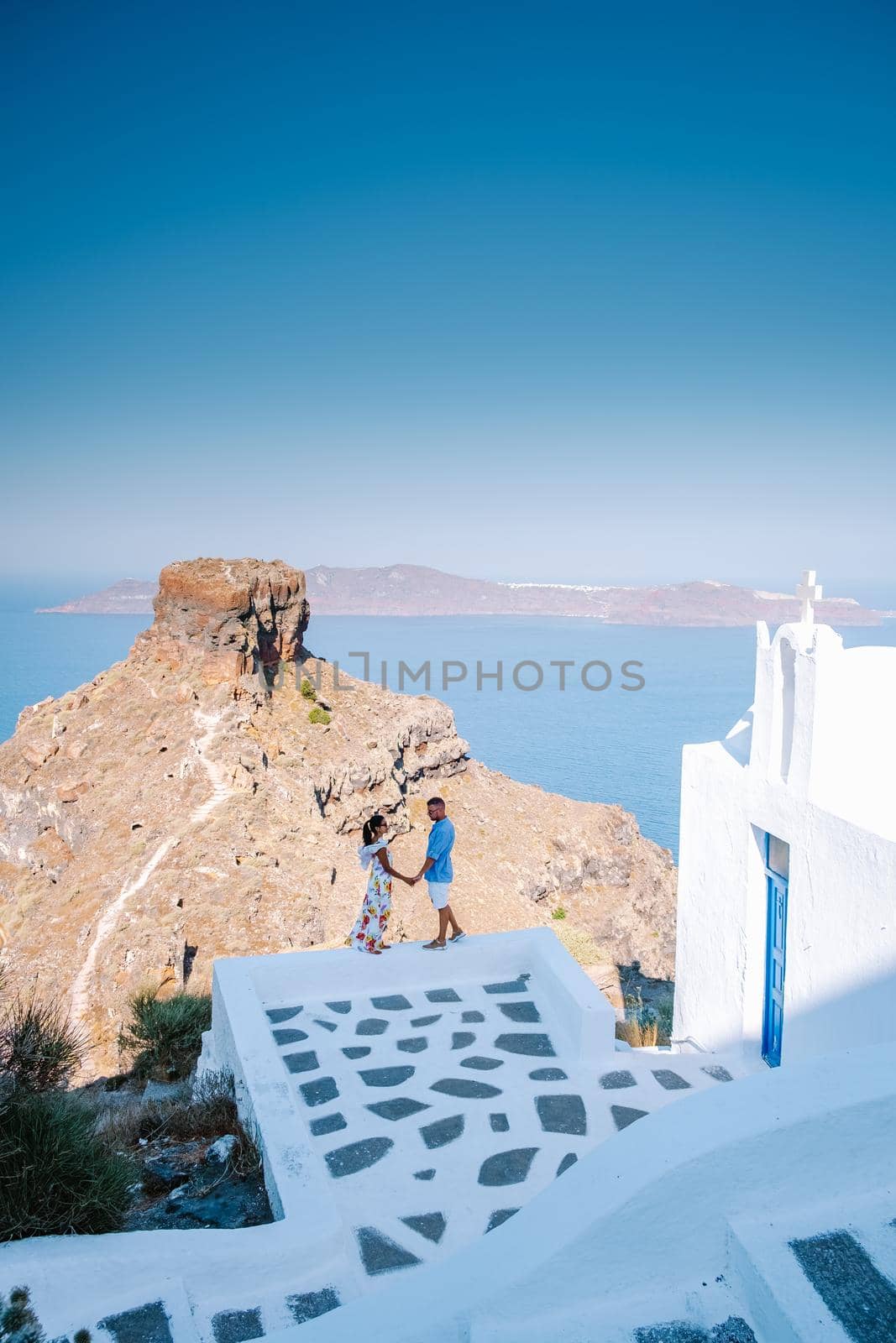 couple visit Skaros rock Fira,Santorini Greece, young couple on luxury vacation at the Island of Santorini watching sunrise by the blue dome church and whitewashed village of Oia Santorini Greece . Europe