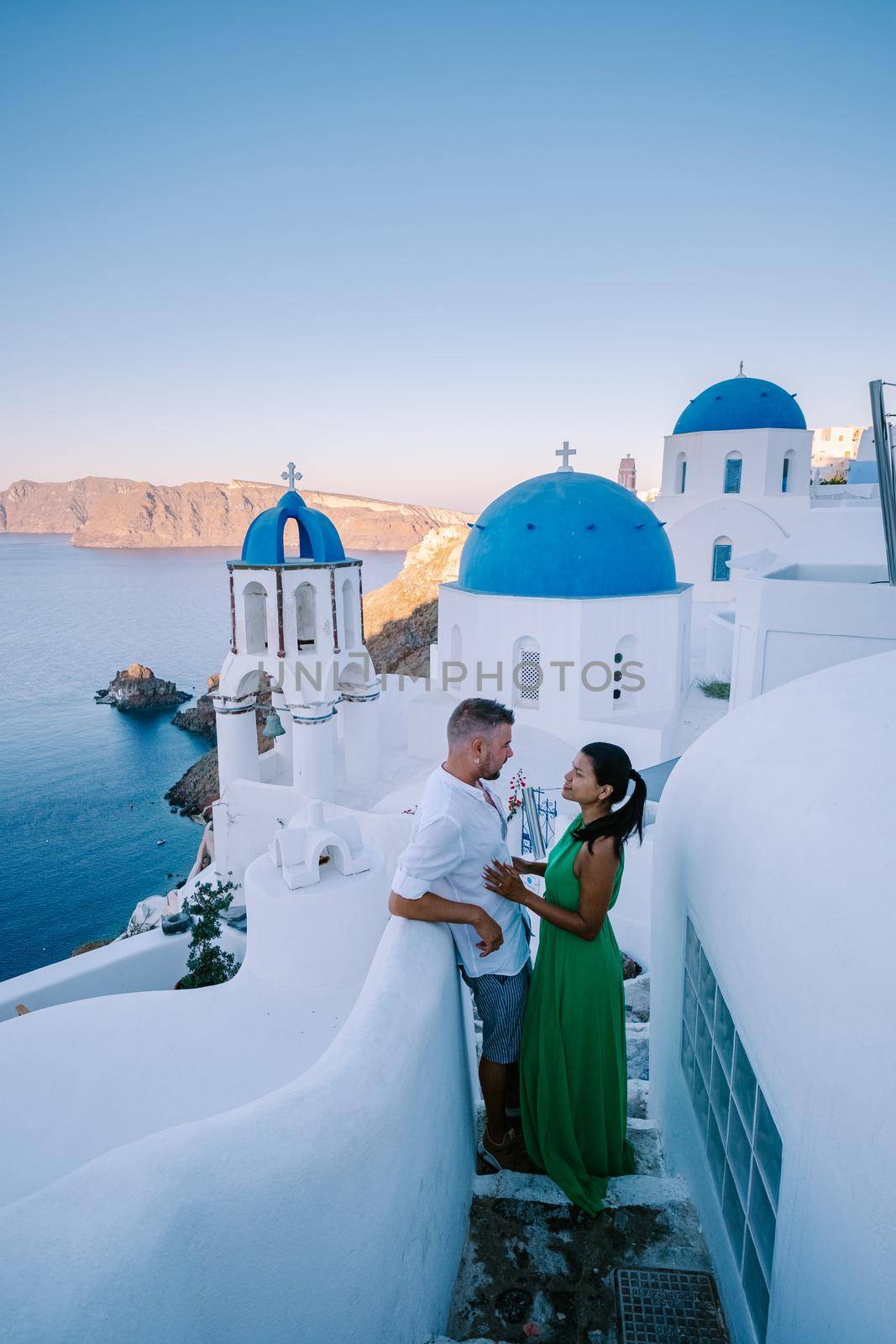 Santorini Greece, young couple on luxury vacation at the Island of Santorini watching sunrise by the blue dome church and whitewashed village of Oia Santorini Greece during sunrise, men and woman on holiday in Greece by fokkebok