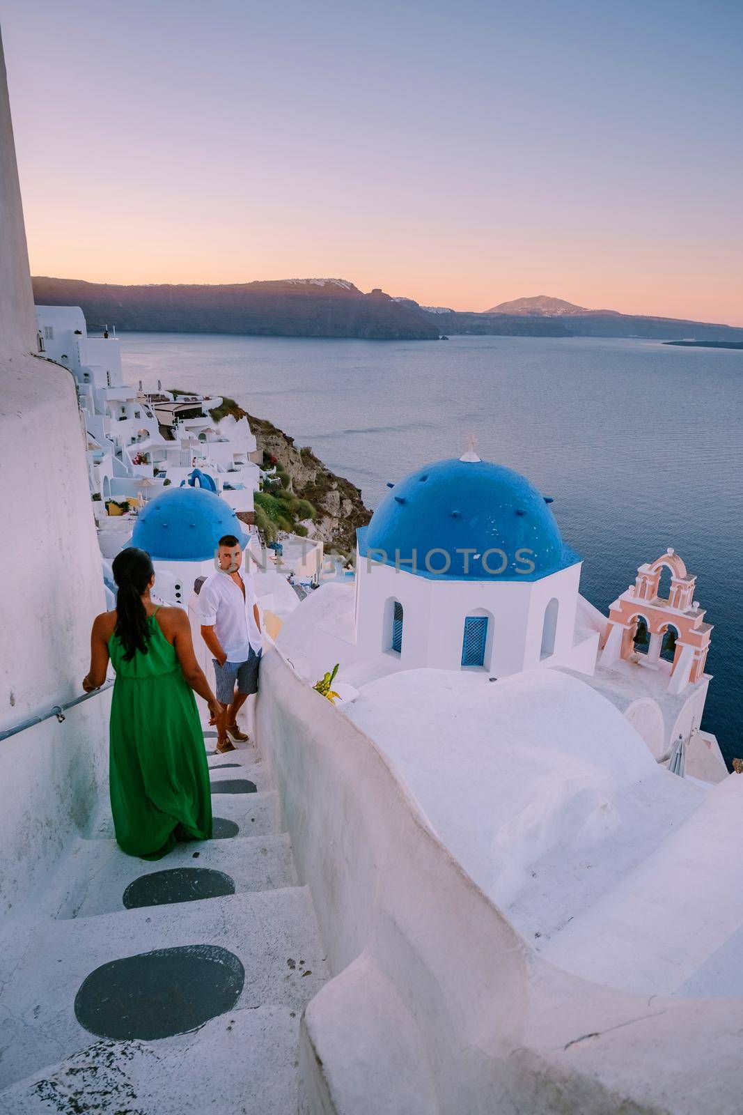 Santorini Greece, young couple on luxury vacation at the Island of Santorini watching sunrise by the blue dome church and whitewashed village of Oia Santorini Greece during sunrise, men and woman on holiday in Greece by fokkebok