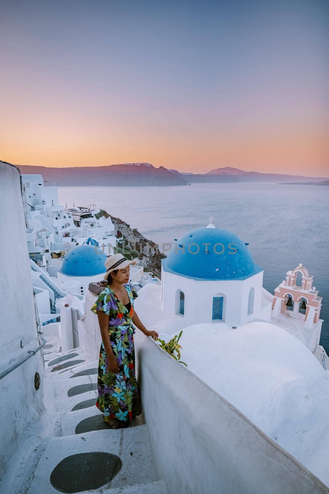 Sunset at the Island Of Santorini Greece, beautiful whitewashed village Oia with church and windmill during sunset, streets of Oia Santorini during summer vacation at the Greek Island Woman on luxury vacation Greece
