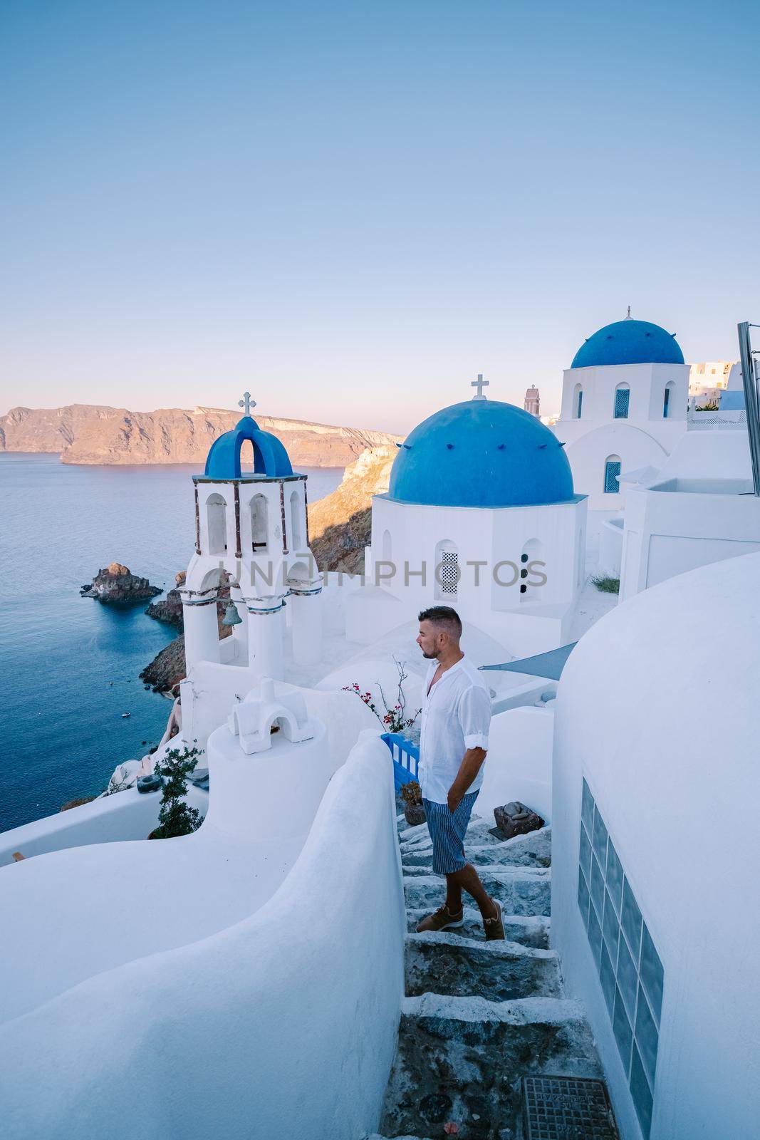 Sunset at the Island Of Santorini Greece, beautiful whitewashed village Oia with church and windmill during sunset, streets of Oia Santorini during summer vacation at the Greek Island, young men on luxury vacation Santorini