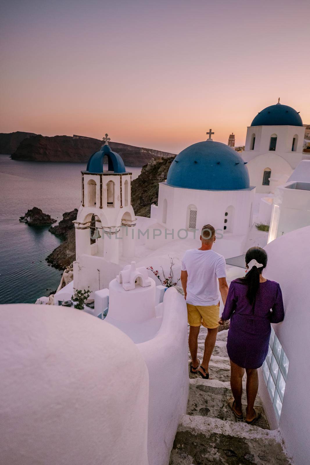 Santorini Greece, young couple on luxury vacation at the Island of Santorini watching sunrise by the blue dome church and whitewashed village of Oia Santorini Greece during sunrise by fokkebok
