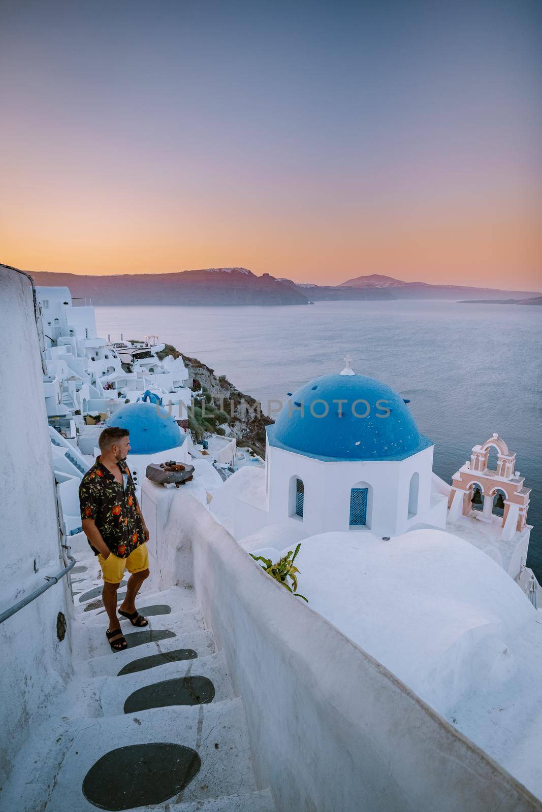 Sunset at the Island Of Santorini Greece, beautiful whitewashed village Oia with church and windmill during sunset, young men on luxury vacation Santorini by fokkebok