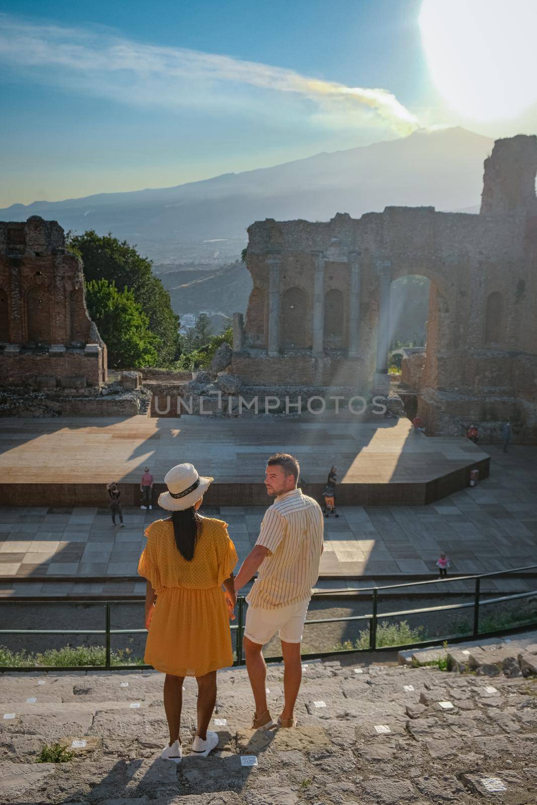 couple men and woman visit Ruins of Ancient Greek theatre in Taormina on background of Etna Volcano, Italy. Taormina located in Metropolitan City of Messina, on east coast of island of Sicily Italy