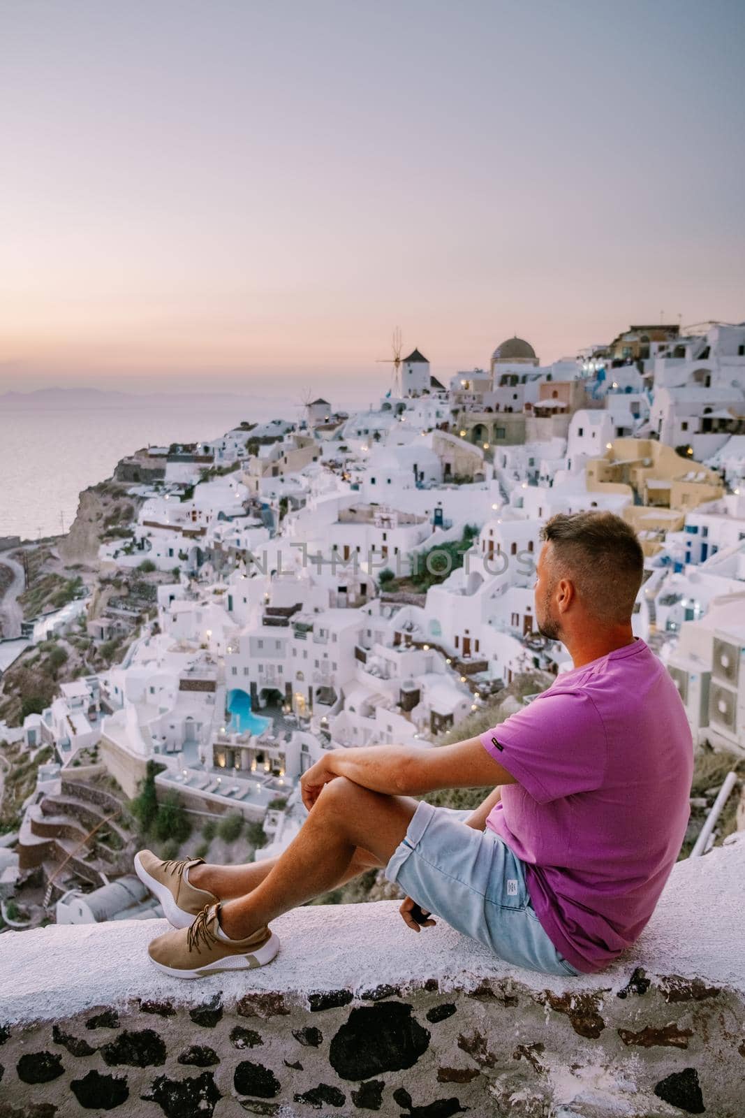 young men watching sunset,Santorini Greece, young couple on luxury vacation at the Island of Santorini watching sunrise by the blue dome church and whitewashed village of Oia Santorini Greece . Europe