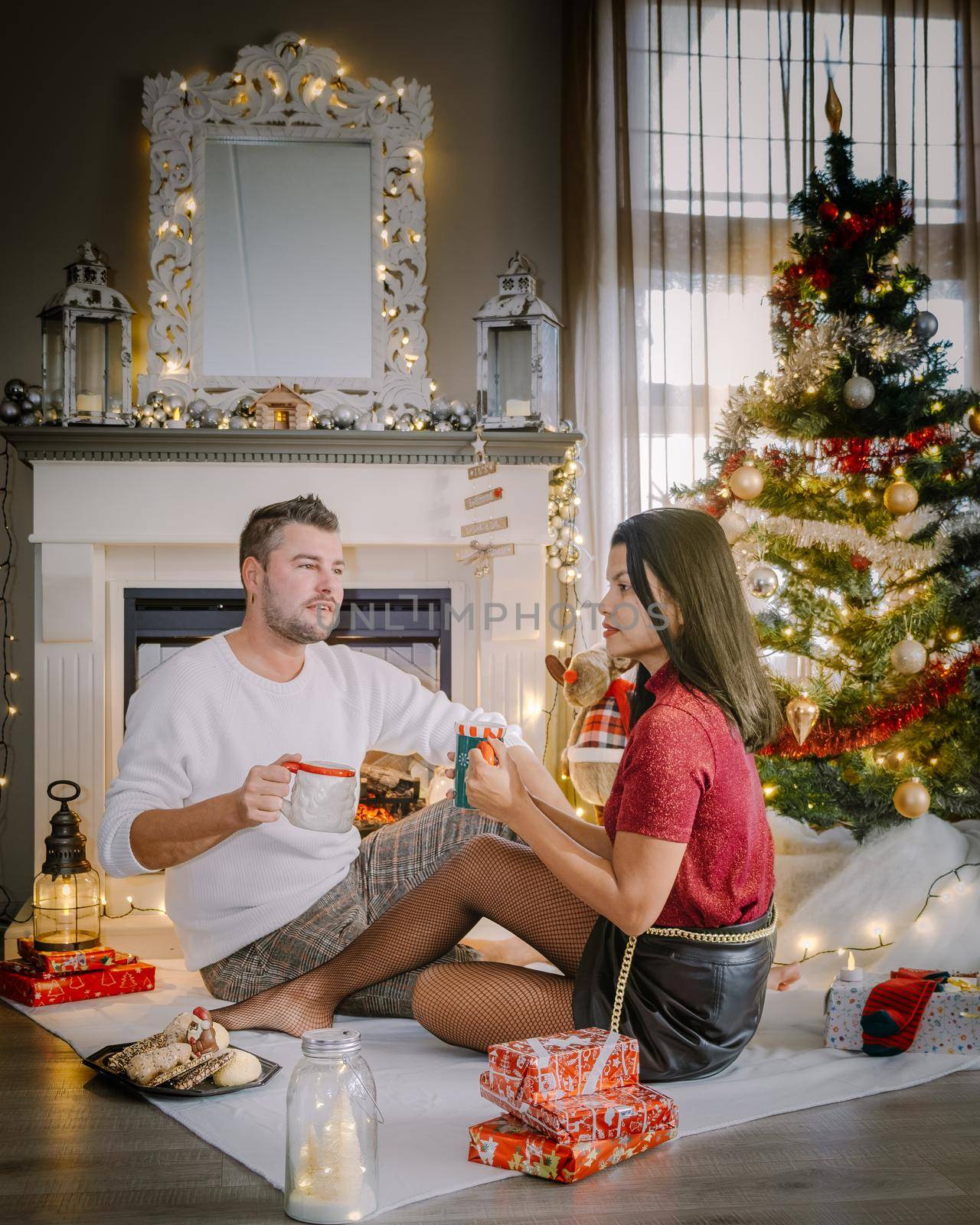 Cute, young couple by fireplace with a Christmas tree,Family sitting on a floor. Couple near christmas tree with candle lights