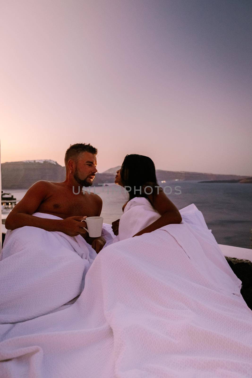 Santorini Greece, young couple on luxury vacation at the Island of Santorini watching sunrise by the blue dome church and whitewashed village of Oia Santorini Greece during sunrise, men and woman on holiday in Greece by fokkebok