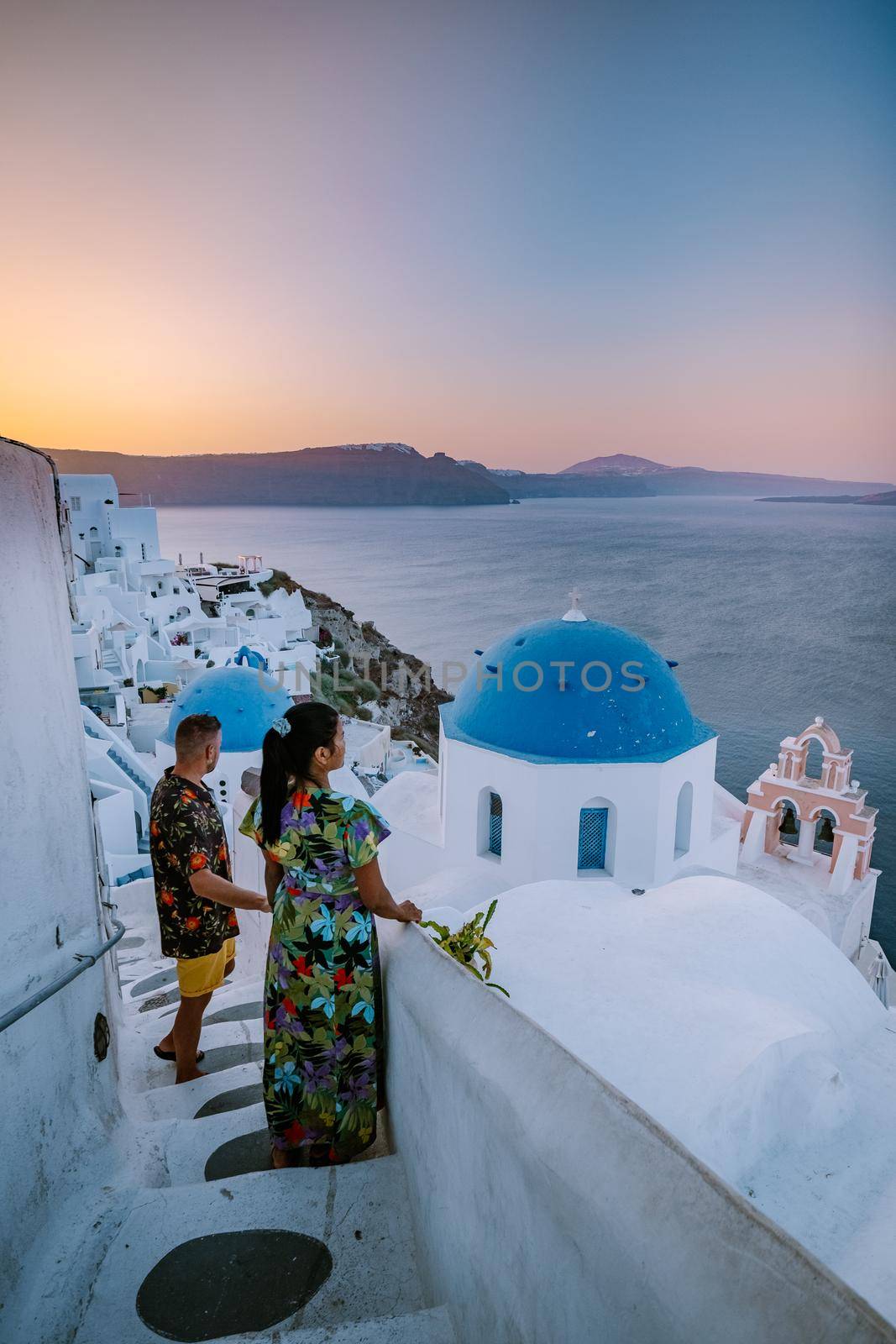 Santorini Greece, young couple on luxury vacation at the Island of Santorini watching sunrise by the blue dome church and whitewashed village of Oia Santorini Greece during sunrise, men and woman on holiday in Greece by fokkebok