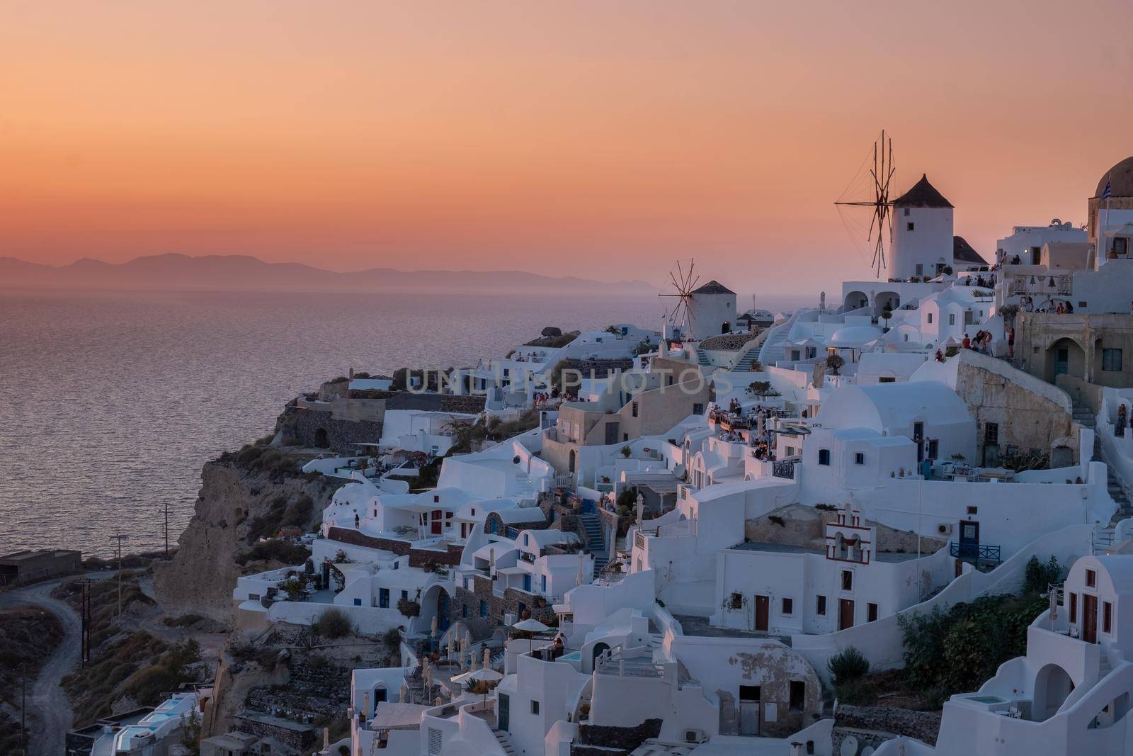 Sunset at the Island Of Santorini Greece, beautiful whitewashed village Oia with church and windmill during sunset, streets of Oia Santorini during summer vacation at the Greek Island