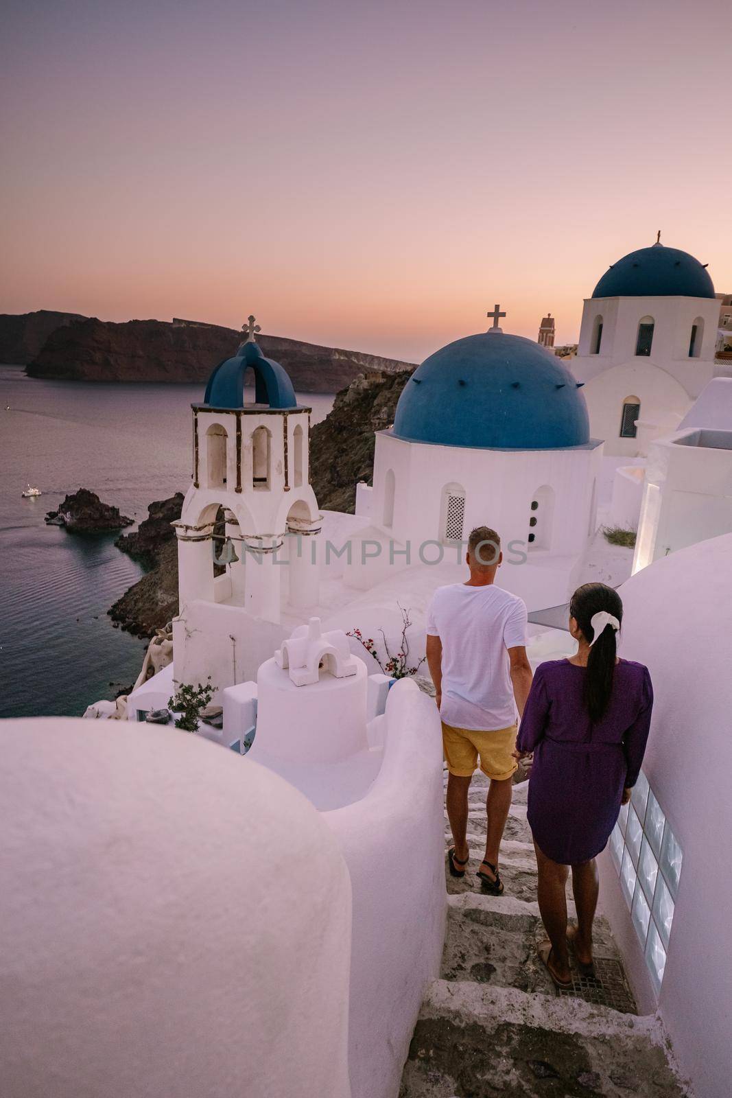 Santorini Greece, young couple on luxury vacation at the Island of Santorini watching sunrise by the blue dome church and whitewashed village of Oia Santorini Greece during sunrise by fokkebok