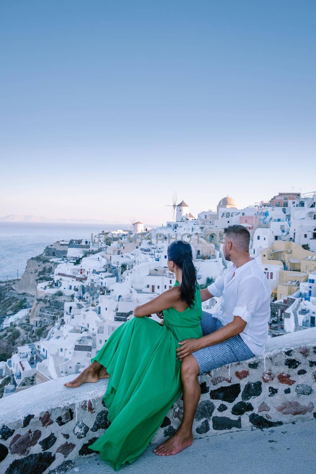 Santorini Greece, young couple on luxury vacation at the Island of Santorini watching sunrise by the blue dome church and whitewashed village of Oia Santorini Greece during sunrise, men and woman on holiday in Greece by fokkebok