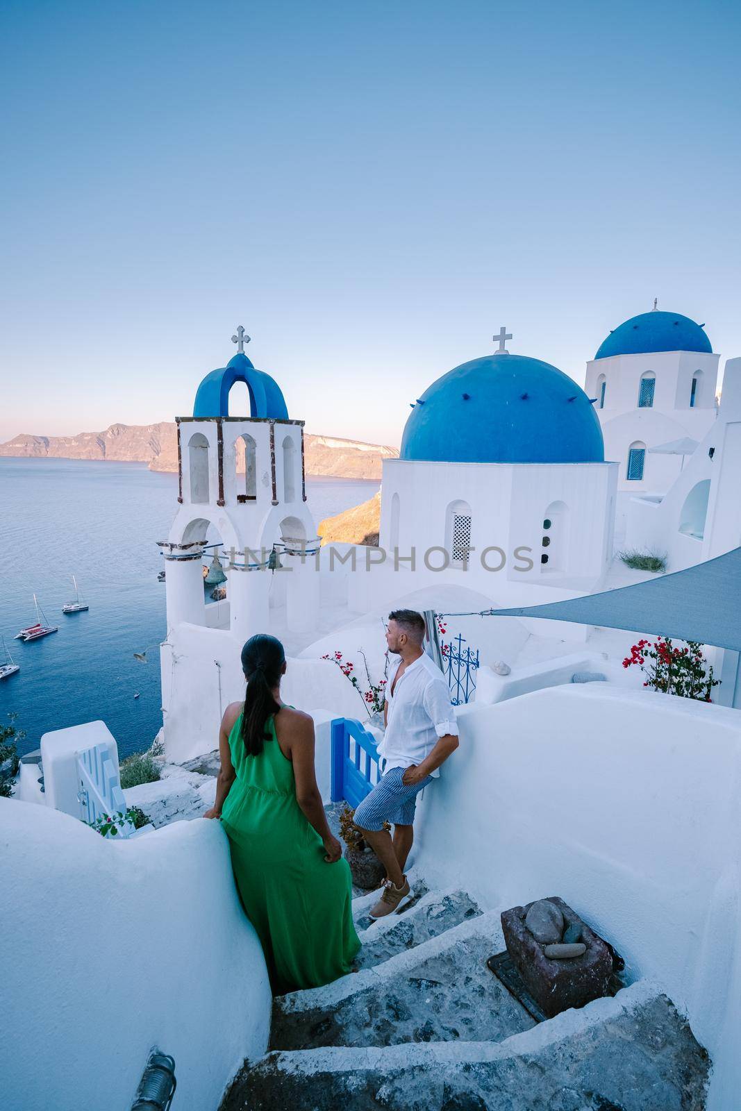 Santorini Greece, young couple on luxury vacation at the Island of Santorini watching sunrise by the blue dome church and whitewashed village of Oia Santorini Greece during sunrise during summer vacation, men and woman on holiday in Greece