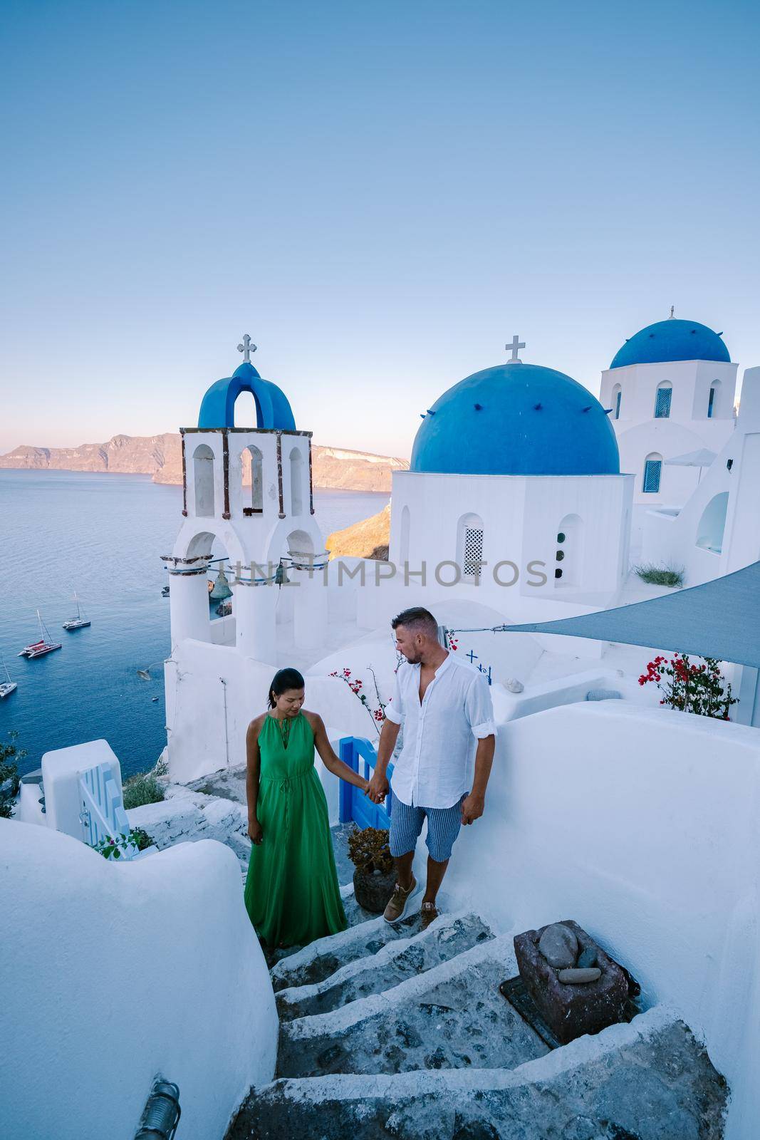 Santorini Greece, young couple on luxury vacation at the Island of Santorini watching sunrise by the blue dome church and whitewashed village of Oia Santorini Greece during sunrise during summer vacation, men and woman on holiday in Greece