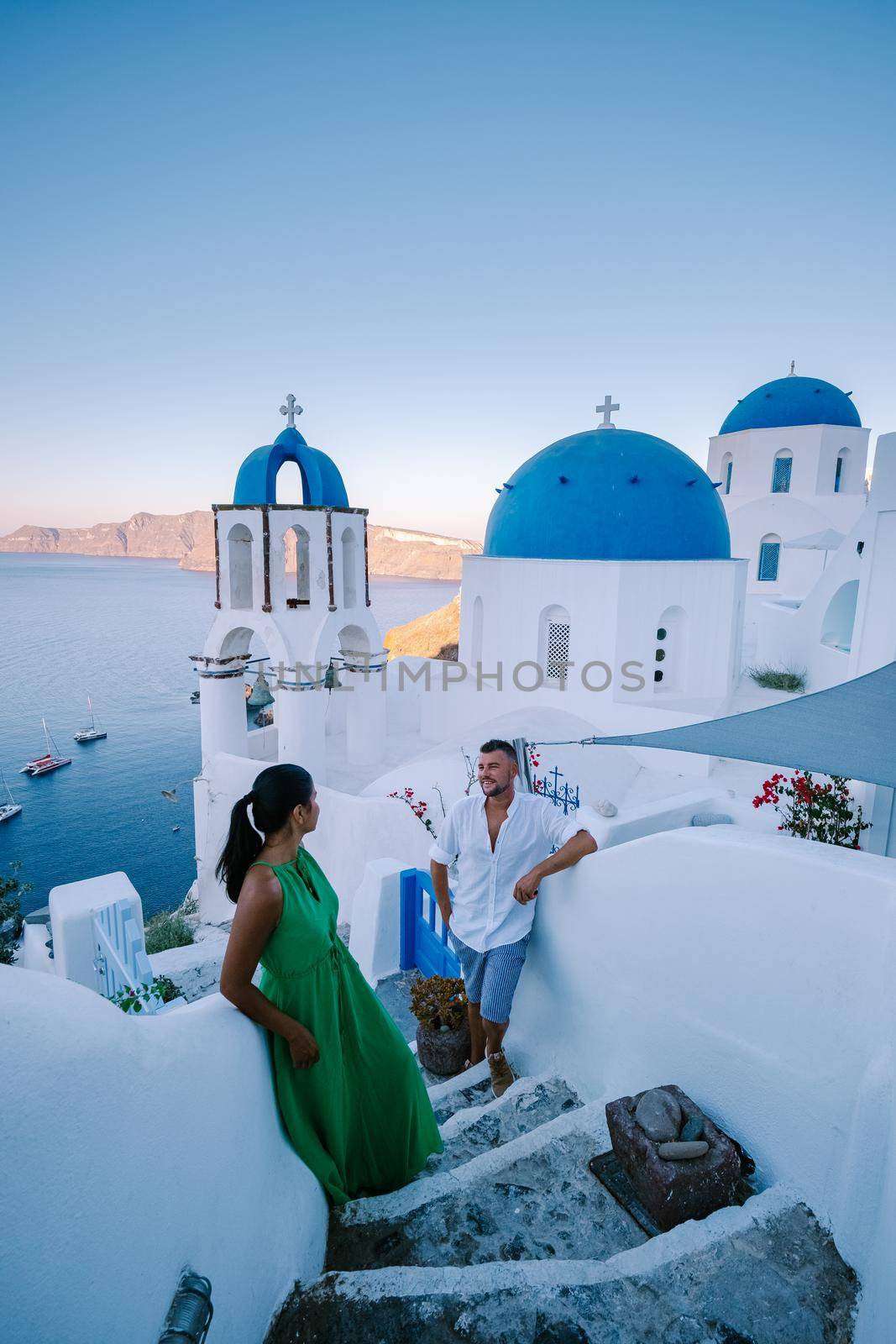 Santorini Greece, young couple on luxury vacation at the Island of Santorini watching sunrise by the blue dome church and whitewashed village of Oia Santorini Greece during sunrise, men and woman on holiday in Greece by fokkebok