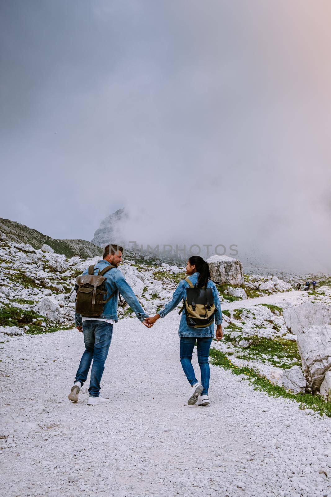 couple hiking in the italian dolomites during foggy weather with clouds, Stunning view to Tre Cime peaks in Dolomites, Italy by fokkebok