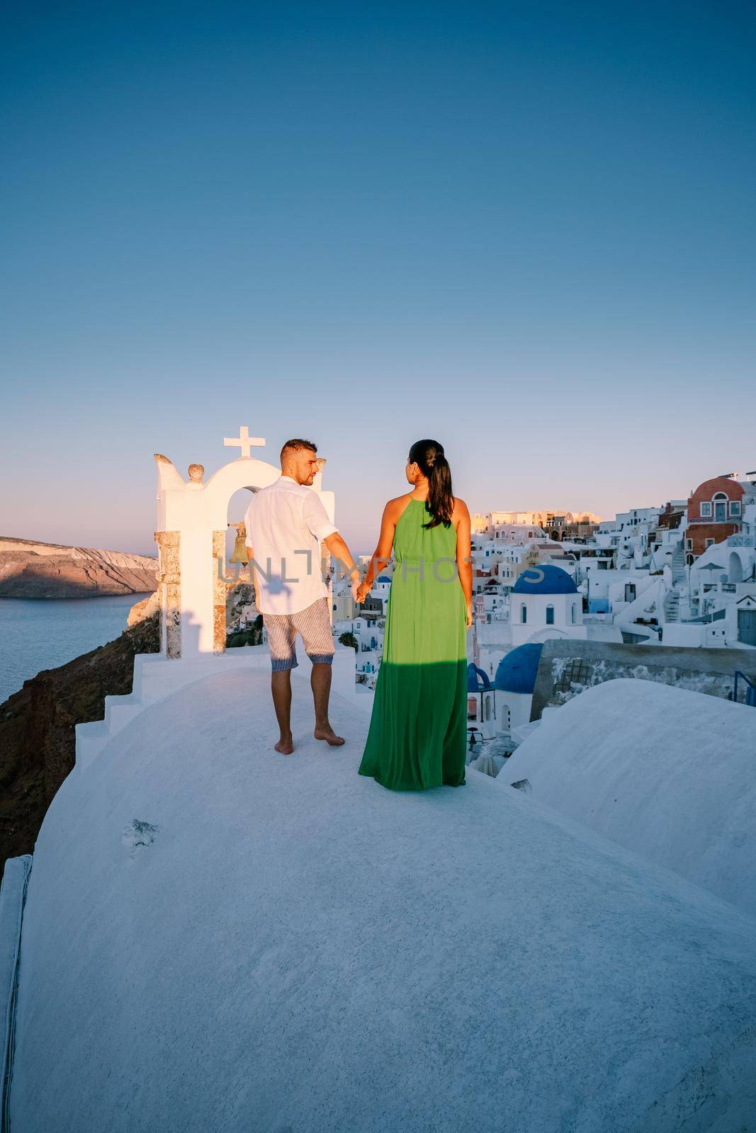 Santorini Greece, young couple on luxury vacation at the Island of Santorini watching sunrise by the blue dome church and whitewashed village of Oia Santorini Greece during sunrise during summer vacation, men and woman on holiday in Greece