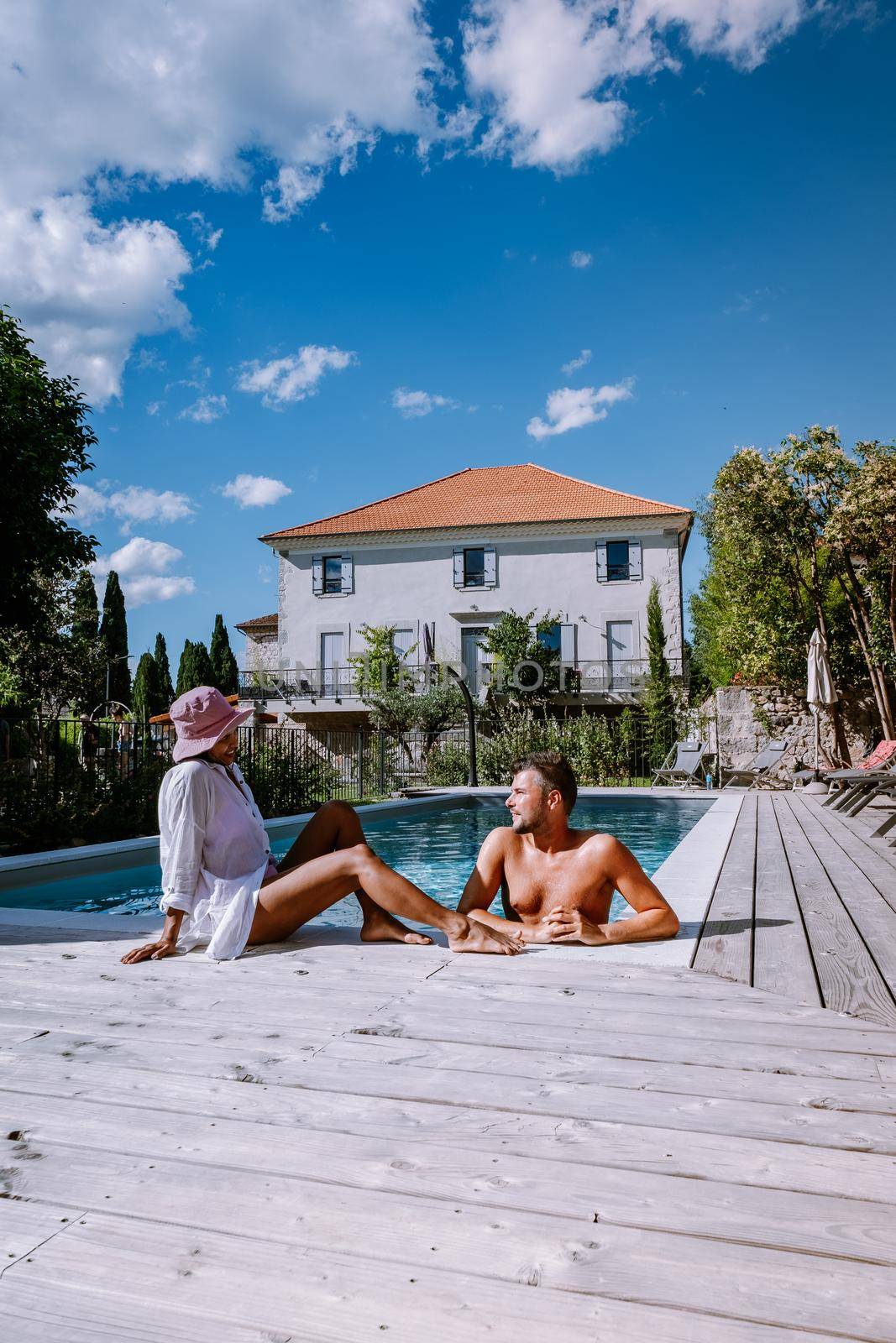 French vacation home with wooden deck and swimming pool in the Ardeche France Europe. Couple relaxing by the pool with wooden deck during luxury vacation at an holiday home in South of France