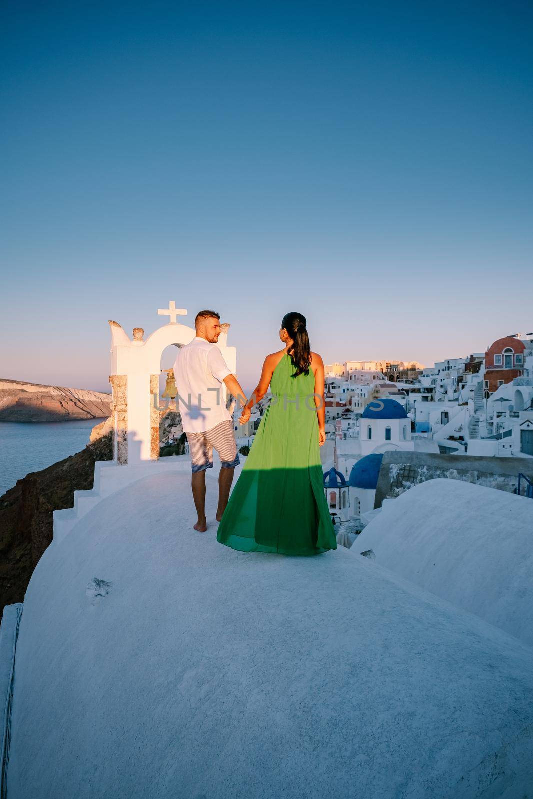 Santorini Greece, young couple on luxury vacation at the Island of Santorini watching sunrise by the blue dome church and whitewashed village of Oia Santorini Greece during sunrise, men and woman on holiday in Greece by fokkebok