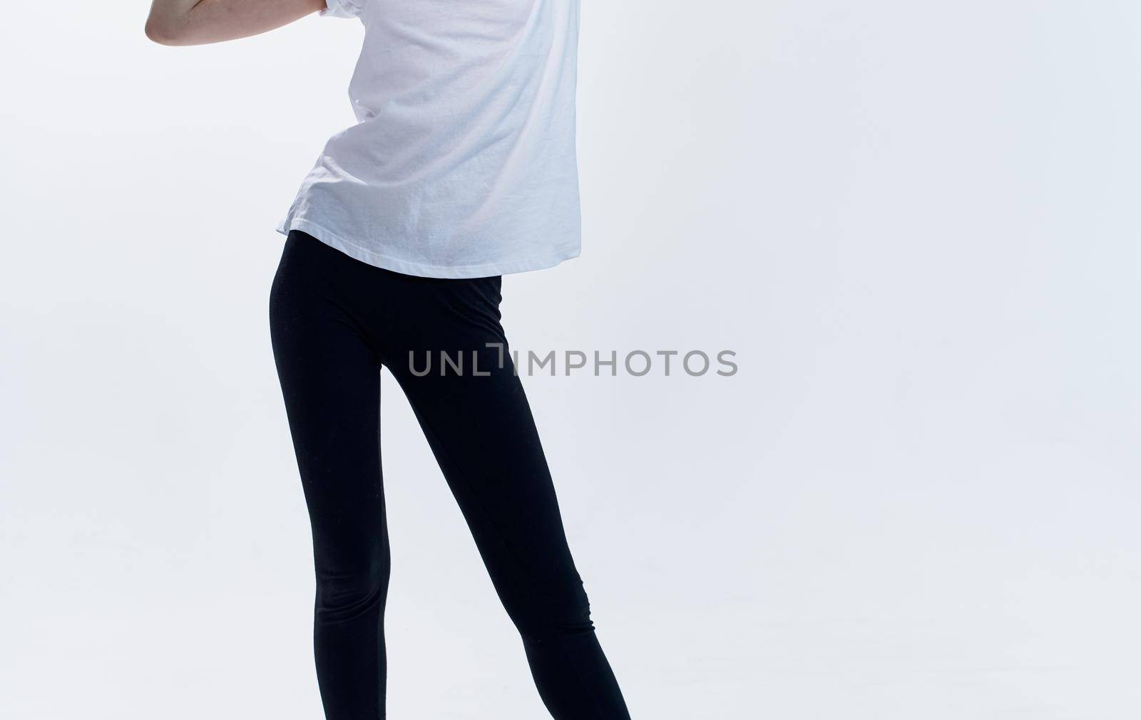 An athletic woman in a white T-shirt and leggings on a light background spread her legs to the sides. High quality photo