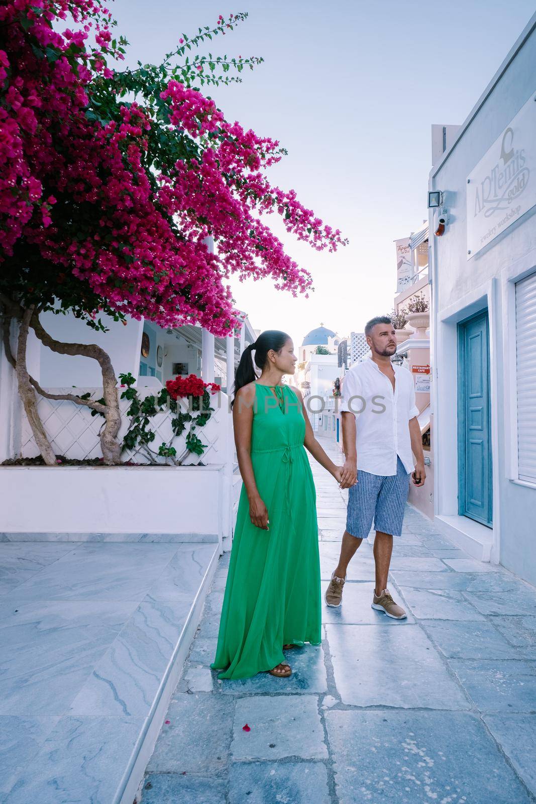 Santorini Greece, young couple on luxury vacation at the Island of Santorini watching sunrise by the blue dome church and whitewashed village of Oia Santorini Greece during sunrise, men and woman on holiday in Greece by fokkebok