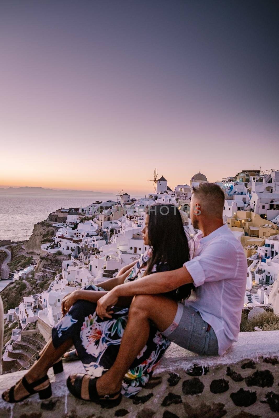 Santorini Greece, young couple on luxury vacation at the Island of Santorini watching sunrise by the blue dome church and whitewashed village of Oia Santorini Greece during sunrise, men and woman on holiday in Greece by fokkebok