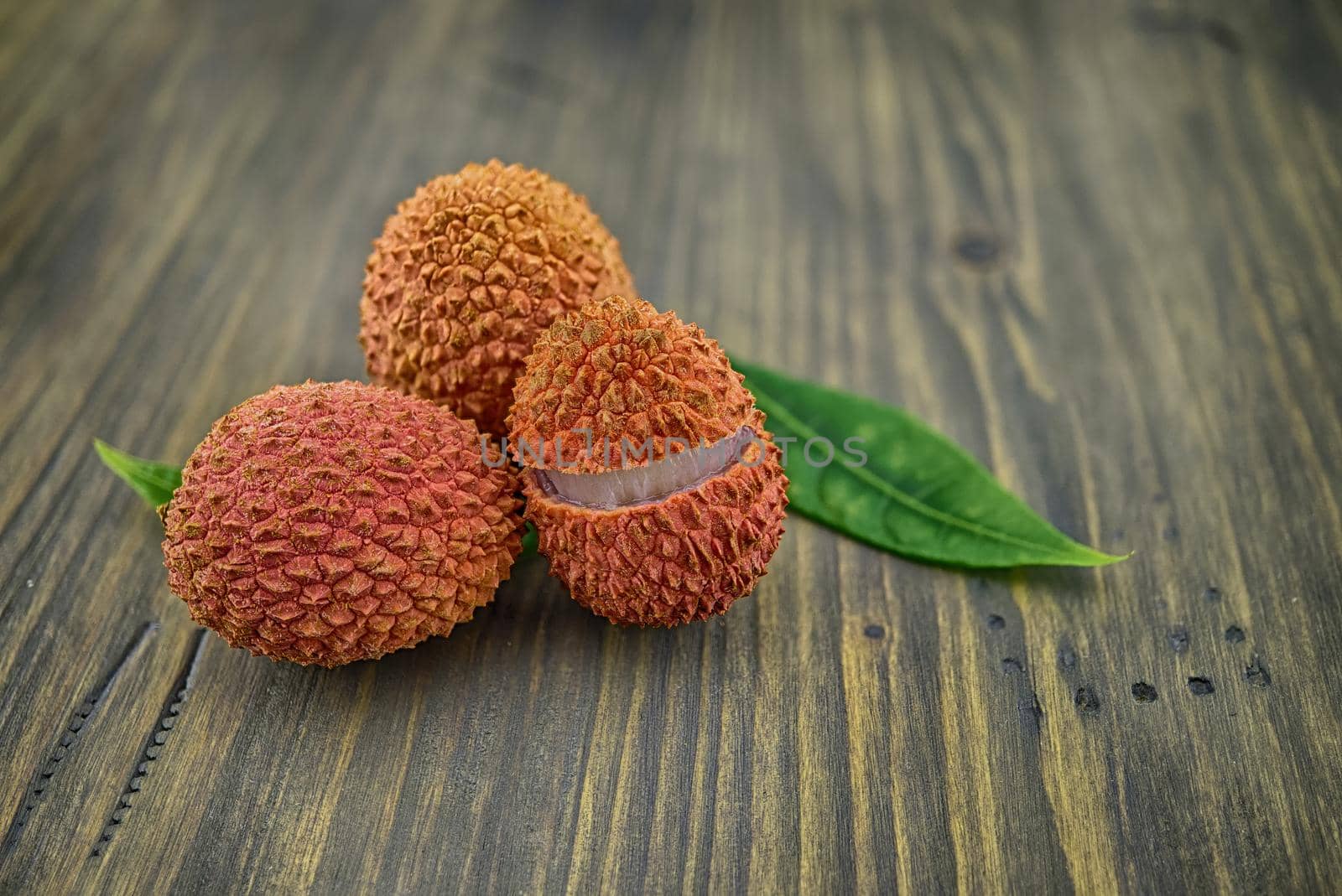 Lychee fruit whole and opened with green leaves decoration on rustic wood background