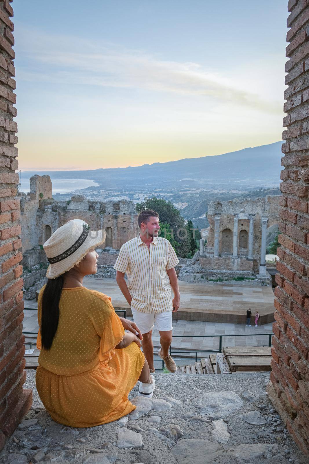 couple men and woman visit Ruins of Ancient Greek theatre in Taormina on background of Etna Volcano, Italy. Taormina located in Metropolitan City of Messina, on east coast of island of Sicily. by fokkebok