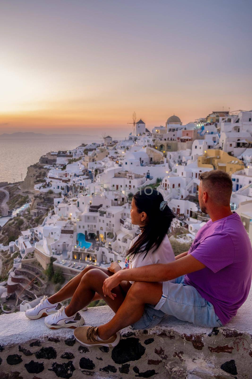 Santorini Greece, young couple on luxury vacation at the Island of Santorini watching sunrise by the blue dome church and whitewashed village of Oia Santorini Greece during sunrise, men and woman on holiday in Greece by fokkebok