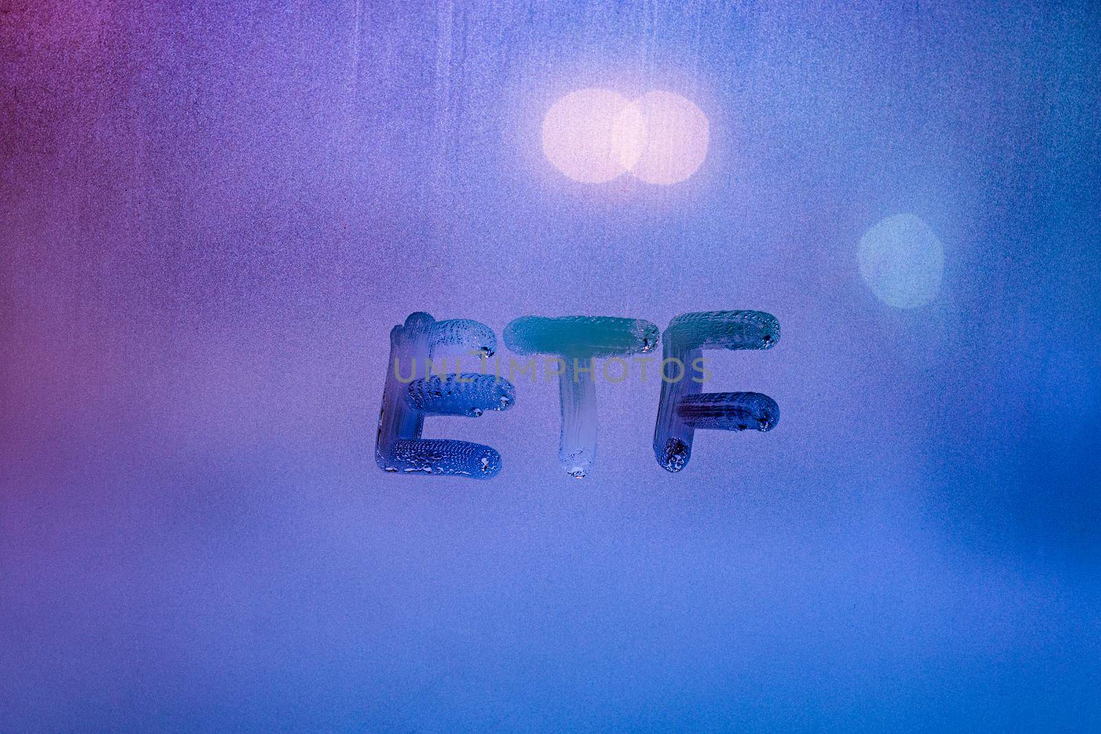 abbreviation word etf - exchange traded funds - handwritten on foggy glass window at night with neon blue back street lights