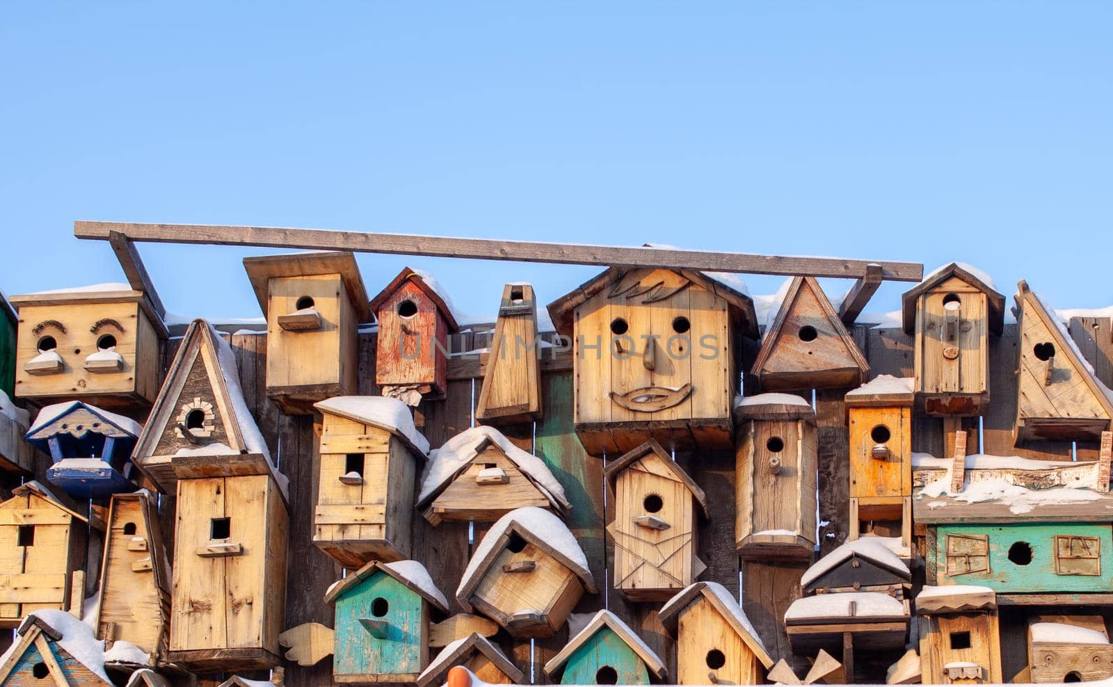 Many different forms of bird feeders. Birdhouses hang on a wooden fence. Bird feeders in the park. Beautiful designer birdhouses for feeding birds. A lot of nesting boxes or houses for feeding the birds.