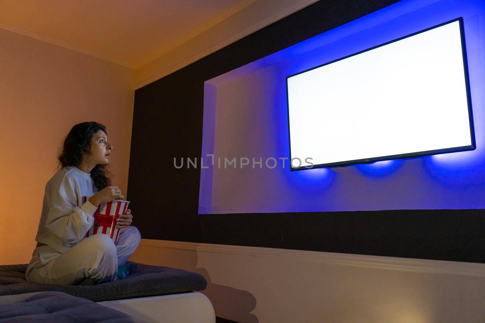 person watches a movie sitting on the couch with a bucket of popcorn.