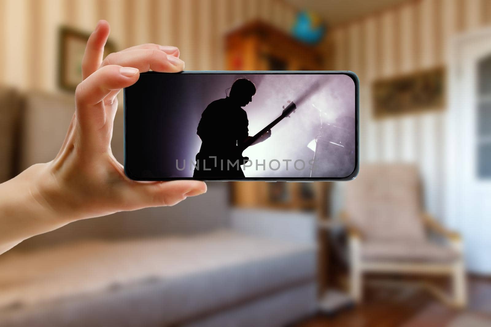 Watching online music concert at home using a mobile phone. Guitarist silhouette on the screen. by 9parusnikov