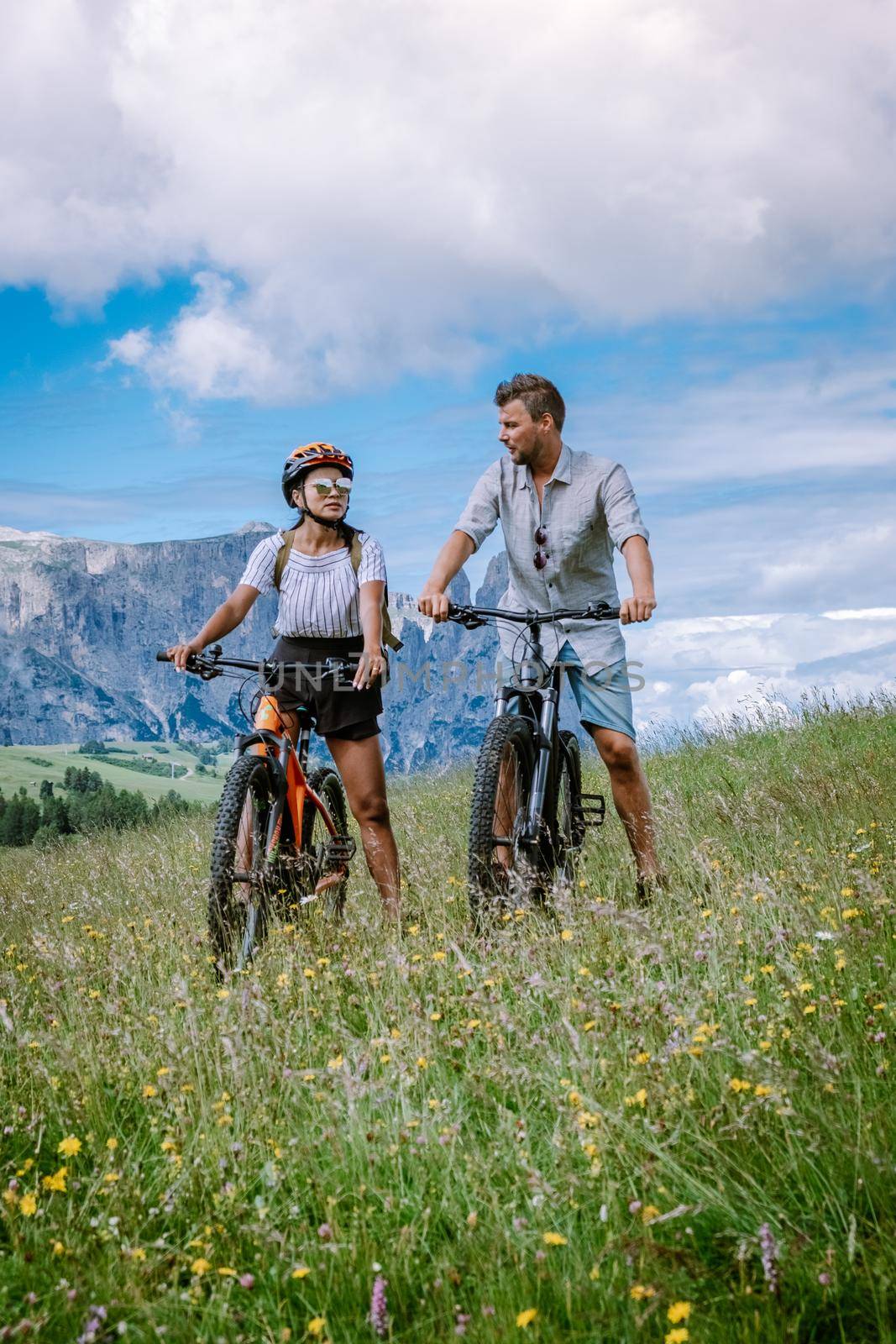 couple men and woman on vacation in the Dolomites Italy, Alpe di Siusi, men and woman on Mountainbike - Seiser Alm with Sassolungo - Langkofel mountain group in background at sunset Europe