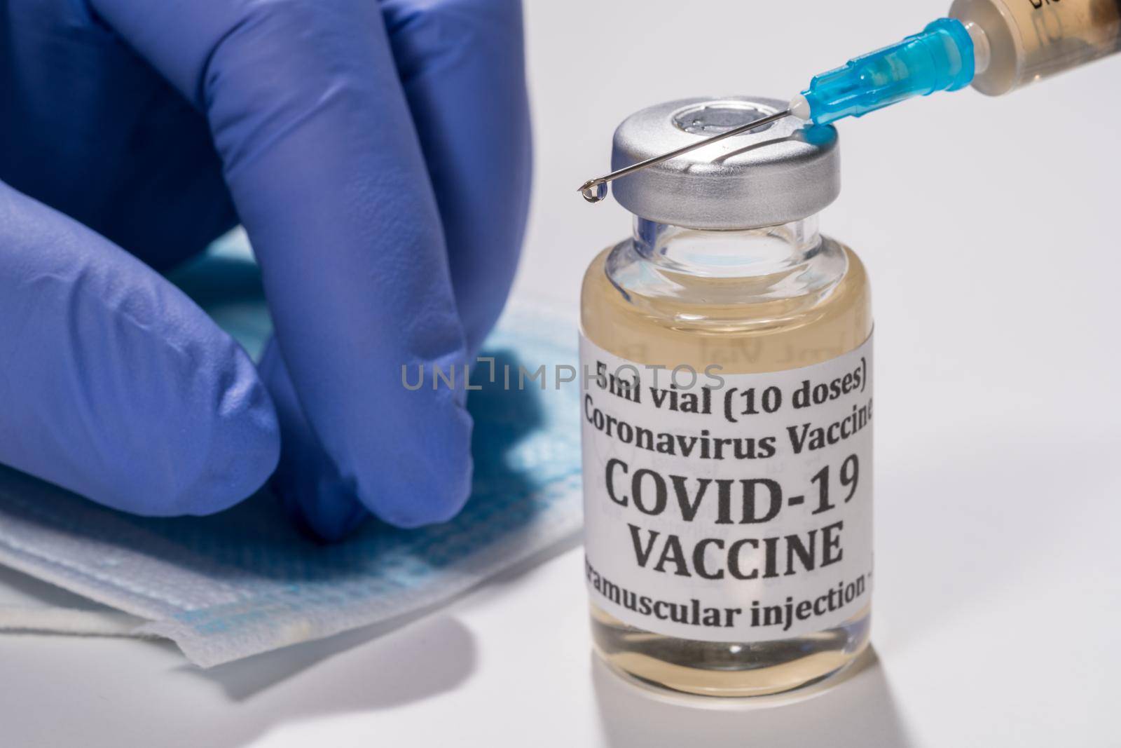 Covid-19 coronavirus vaccine with hypodermic syringe needle with droplet of liquid on tip. Gloved hand in background