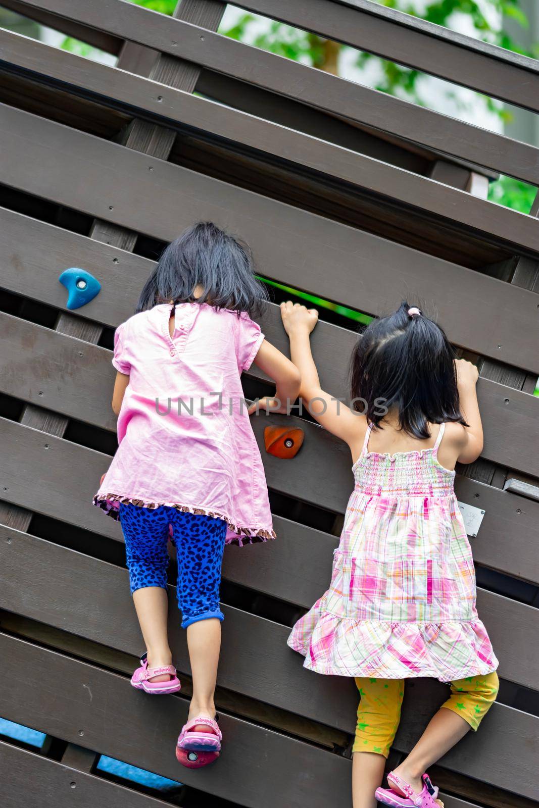 Pretty asian little twins girls while climbing in a playground and helping each other