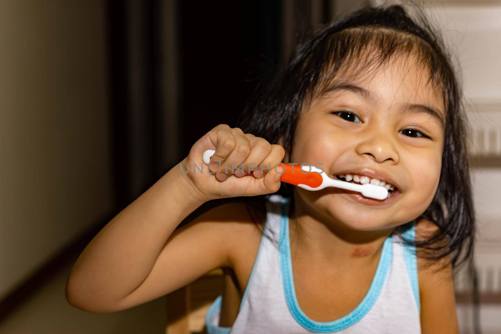 Little asian girl kid while brushing her teeth. Child while enjoying brushing her teeth