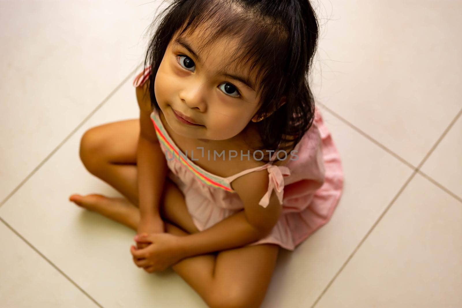 Cute little asian girl sitting on a floor and looking up