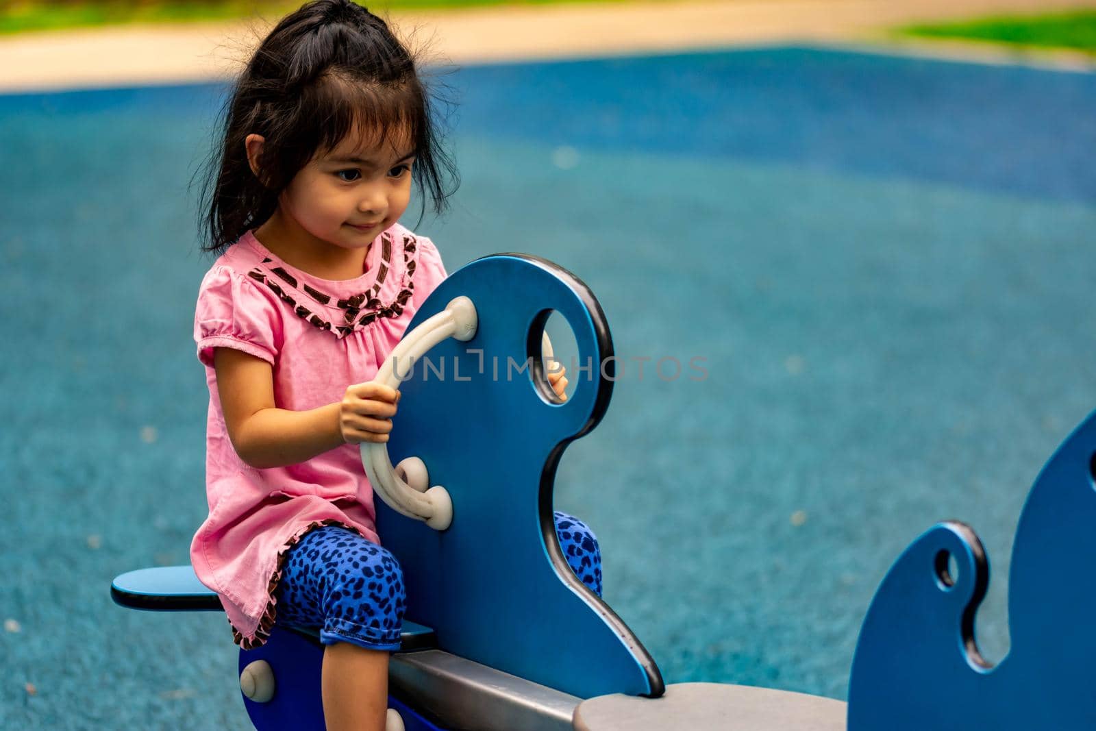 Pretty asian little girl while sitting and playing on a see saw in a playground