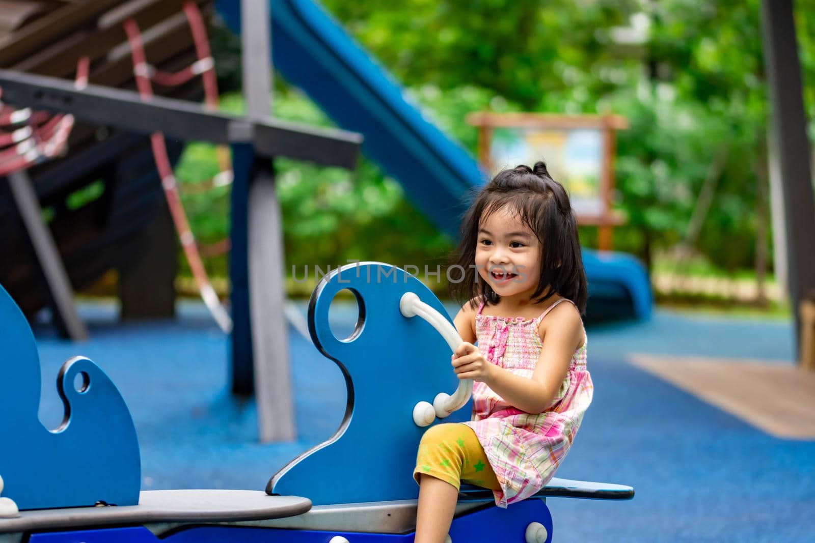 Pretty asian little girl while sitting and playing on a see saw in a playground