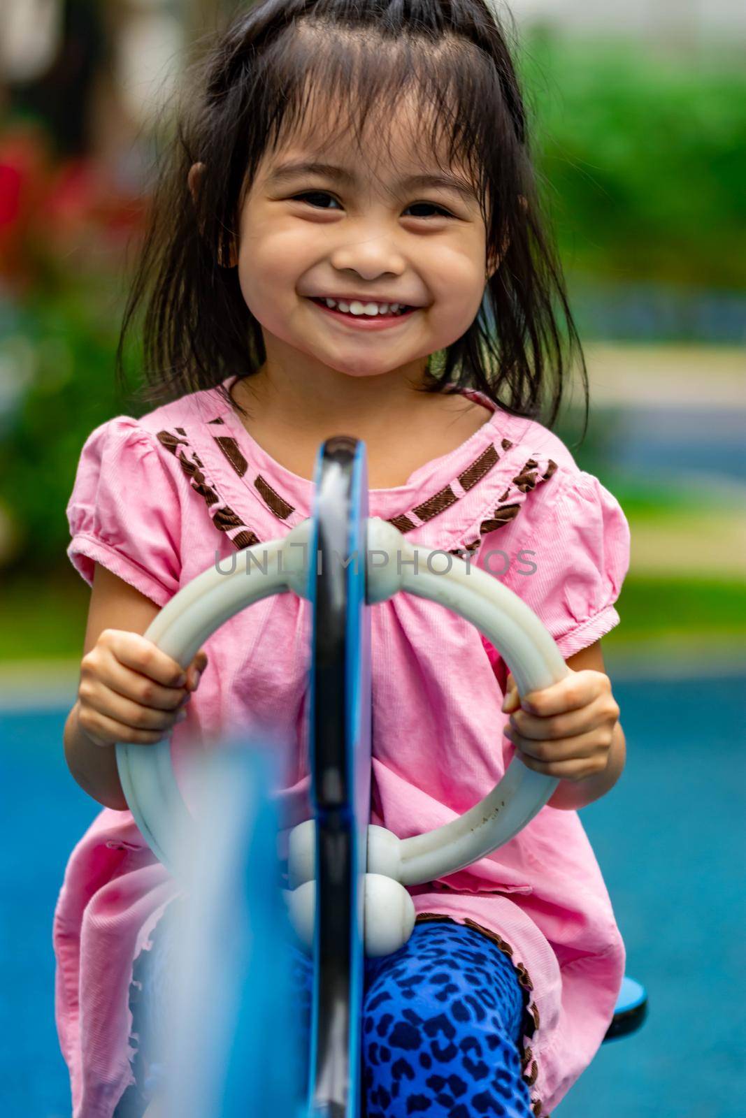 Pretty asian little girl while sitting and playing on a see saw in a playground