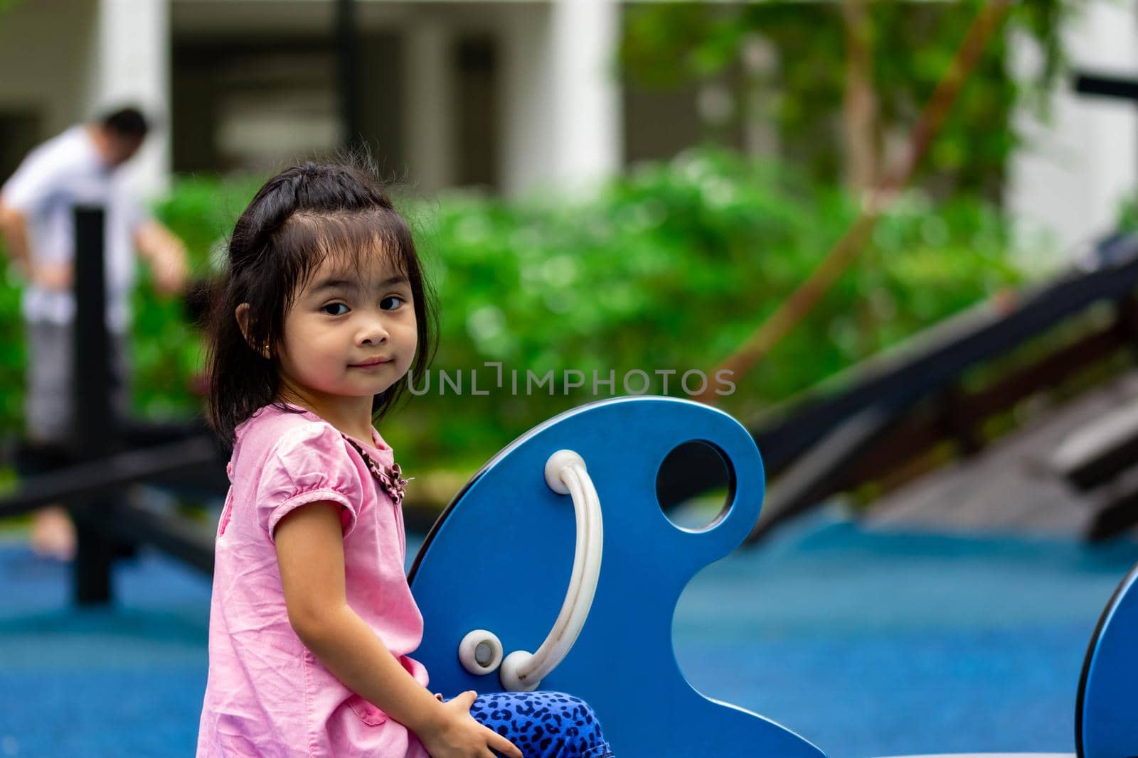 Pretty asian little girl while sitting and playing on a see saw in a playground
