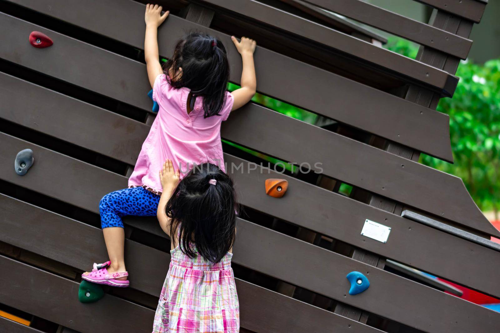 Pretty asian little twins girls while climbing in a playground and helping each other