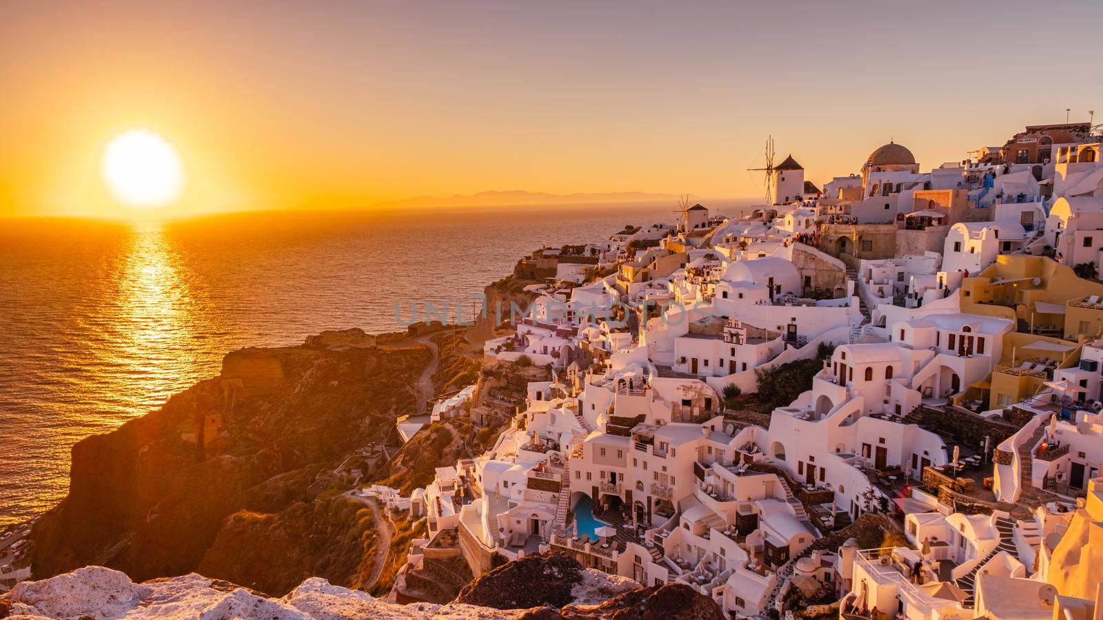 Sunset at the Island Of Santorini Greece, beautiful whitewashed village Oia with church and windmill during sunset by fokkebok