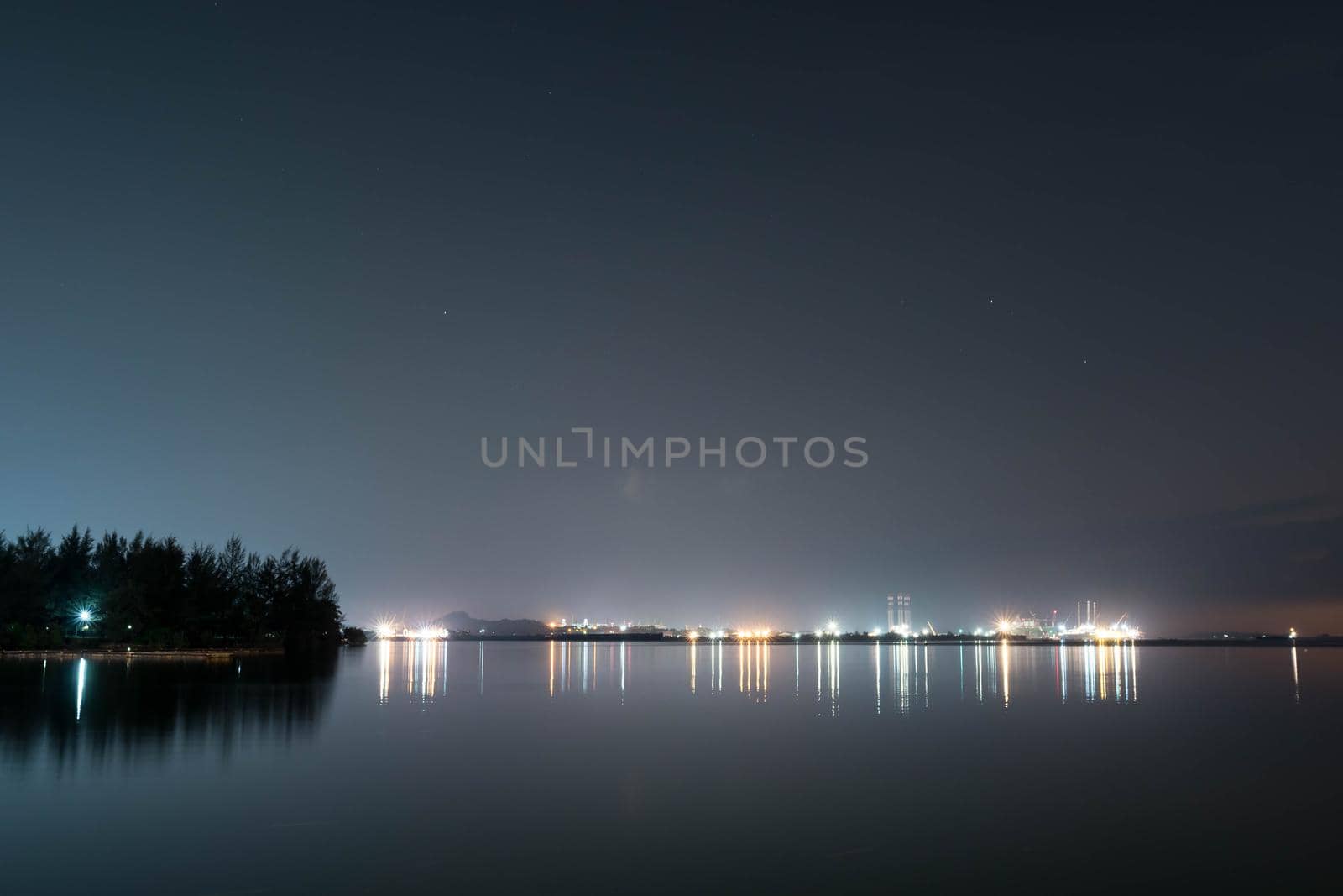 Coastline view of sea, pier, sky during dusk with lights reflection on water somewhere in Asia