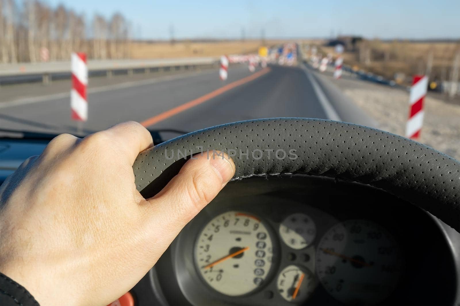 the driver hand on the steering wheel of the car and the dashboard on the background of the road being repaired with fences, columns indicating the path of the detour