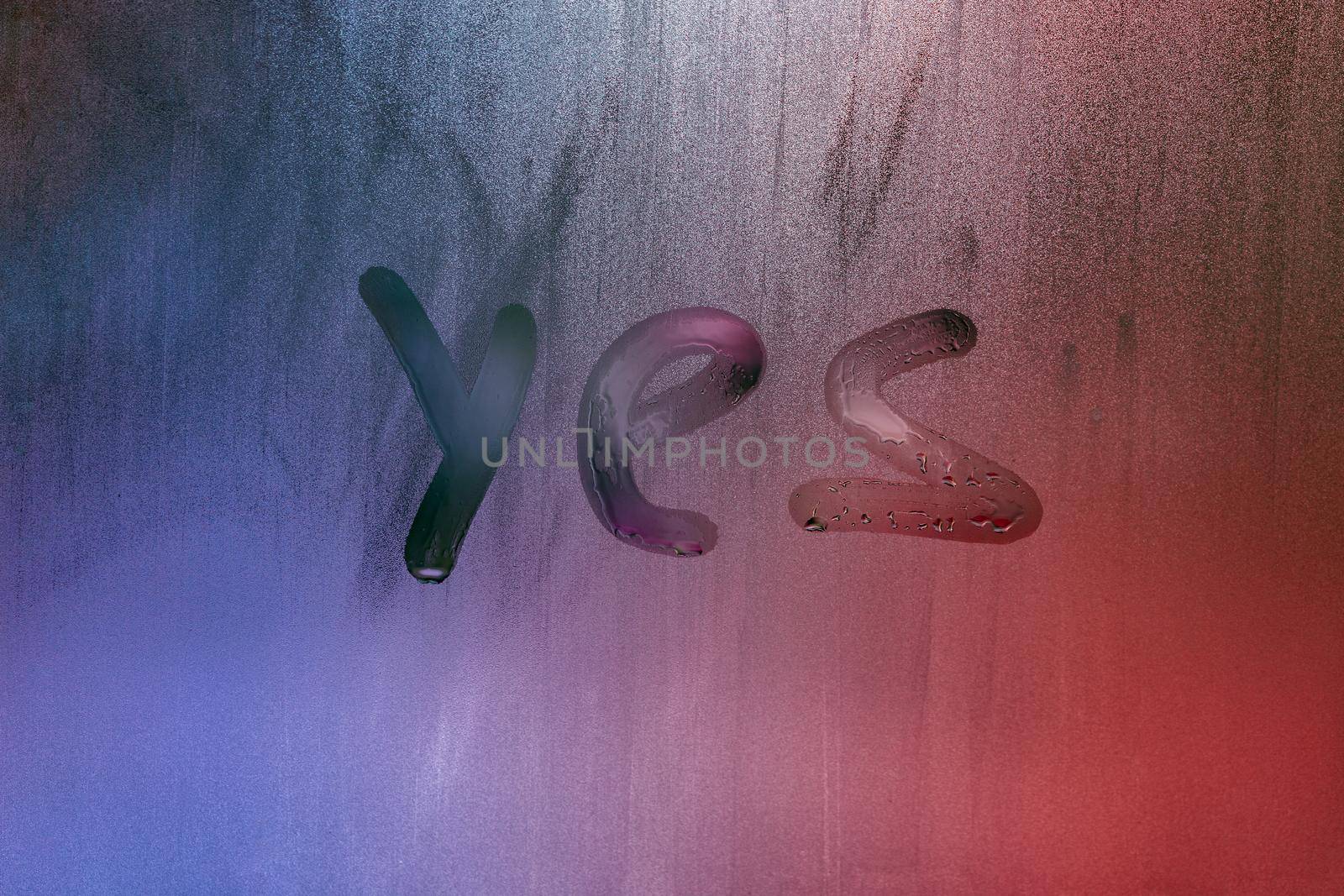 word yes handwritten on foggy night window glass surface, close-up with selective focus